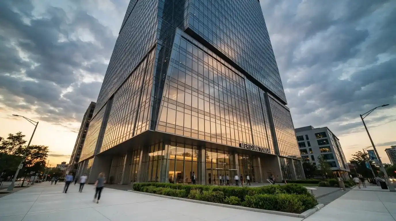 Un edificio de oficinas con fachada de cristal reflejando nubes, fotografiado desde una acera ancha por la tarde.